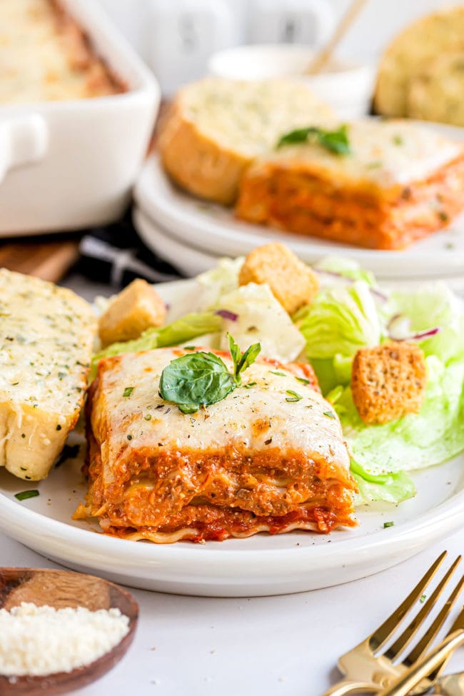 serving of lasagna on a plate with salad and cheese garlic bread