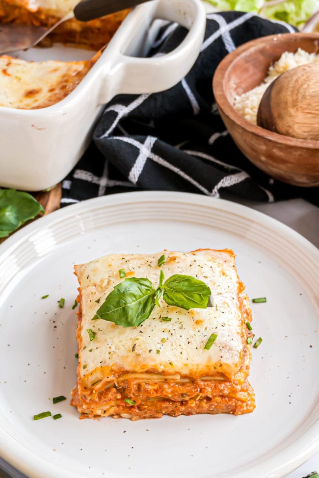 Serving of beef and ricotta lasagna on a white plate with fresh basil garnish