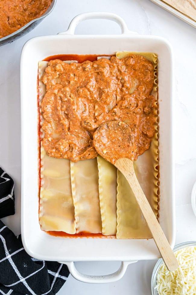 layering meat sauce and cheese with lasagna noodles in a white baking dish