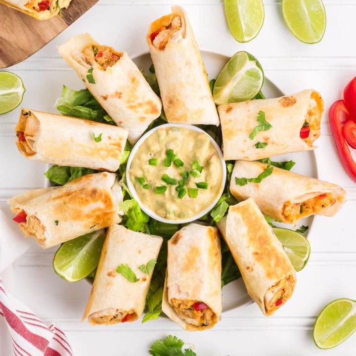 firecracker chicken wraps on a round platter with a bowl of avocado sauce in the center