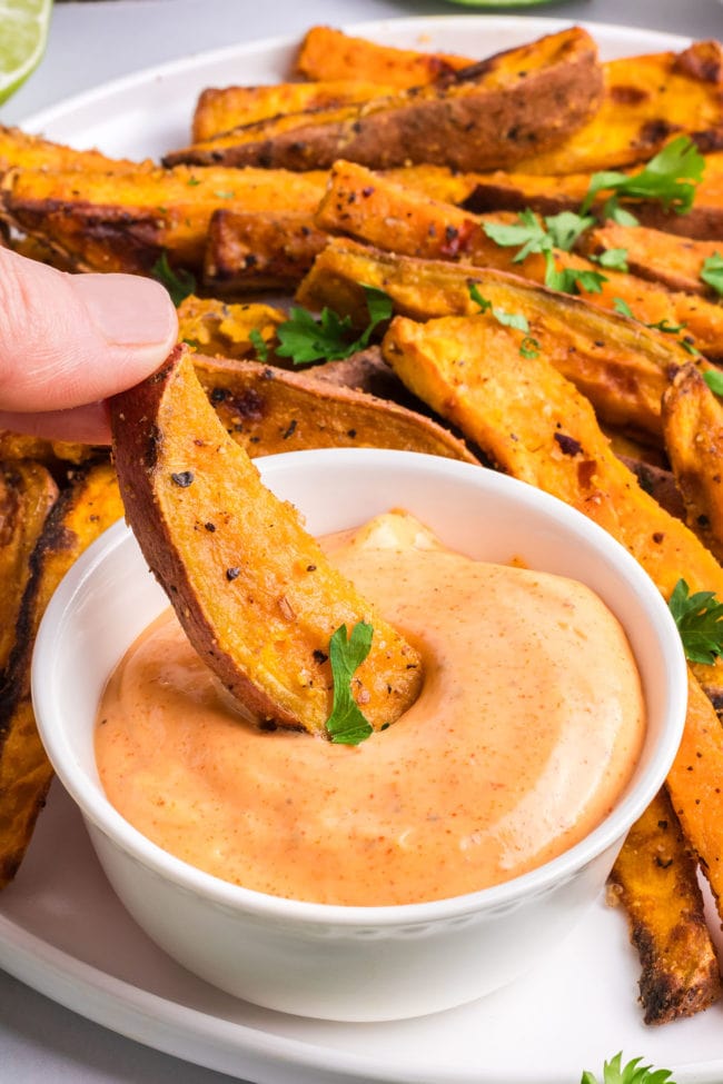 dipping a sweet potato wedge in zesty mayo sauce