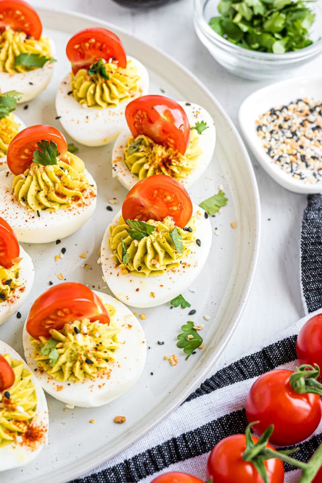 deviled eggs with cherry tomato on top on a white plate