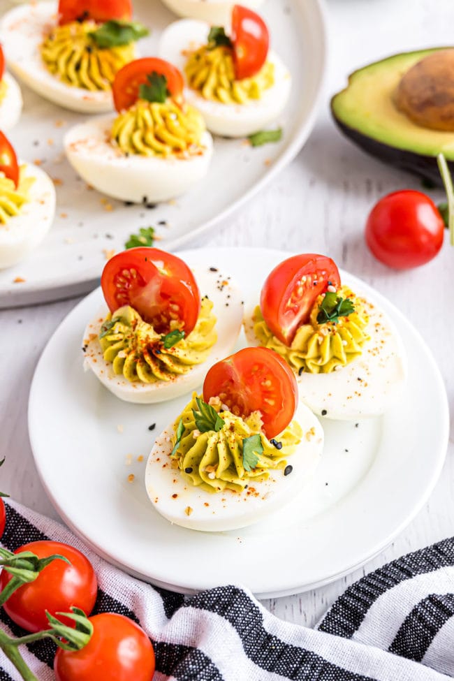3 deviled avocado deviled eggs with tomatoes on a white plate