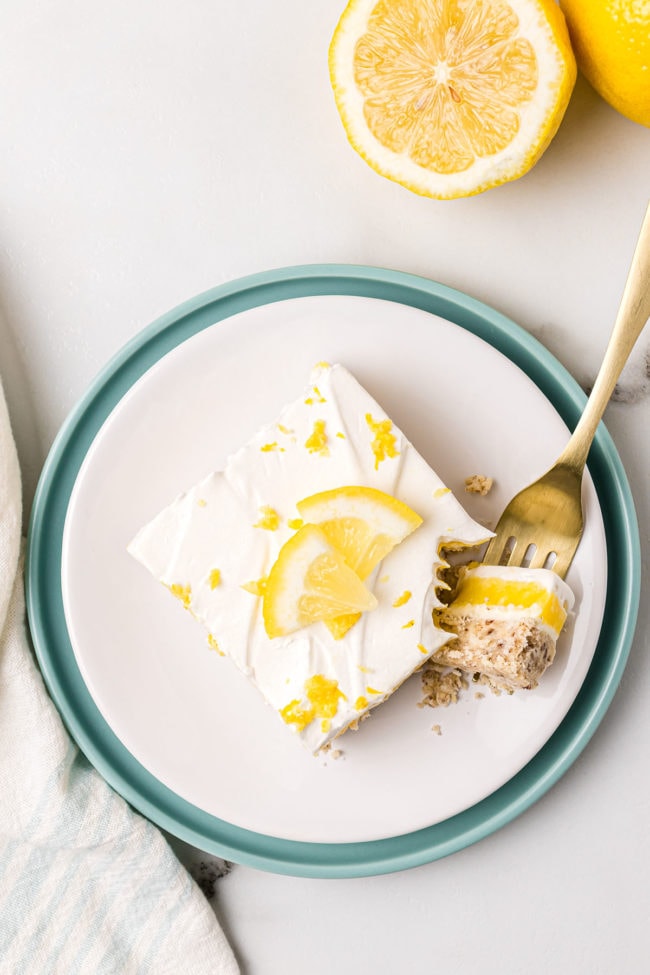 Flat lay of a serving on lemon lush dessert on a white plate with fresh lemon slice for garnish