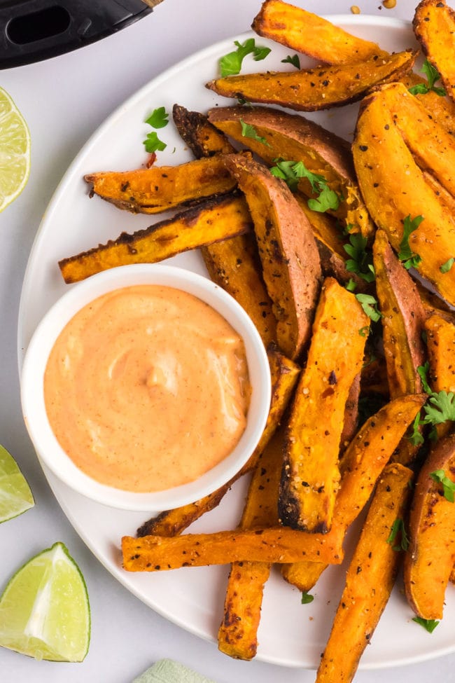 Plate of Air Fryer Crispy sweet potato wedges on a platter with spicy mayo dipping sauce.