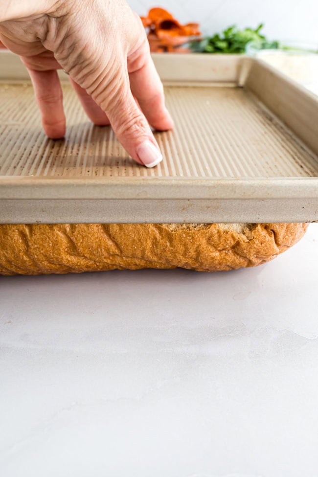 smashing down bread loaf with baking sheet for bread pizza