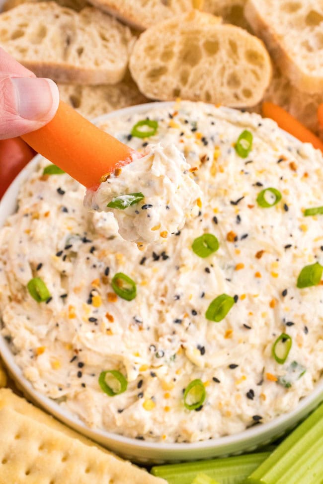 dipping a carrot into a bowl of everything but the bagel dip