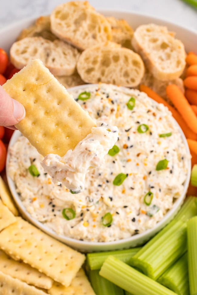 dipping a cracker into a bowl of everything bagel dip