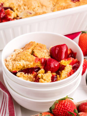 strawberry dump cake in a stack of bowls next to a white baking dish