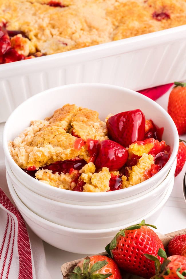 strawberry dump cake in a stack of bowls next to a white baking dish