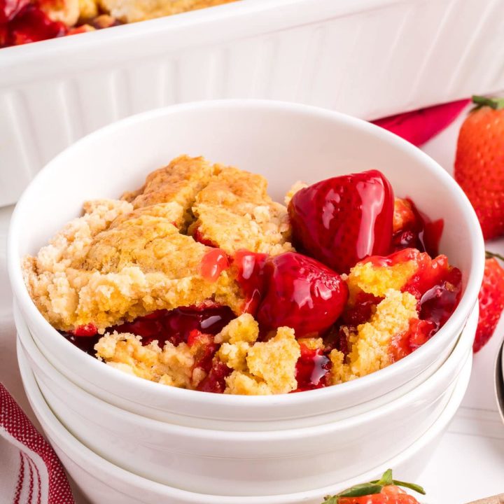 strawberry dump cake in a stack of bowls next to a white baking dish