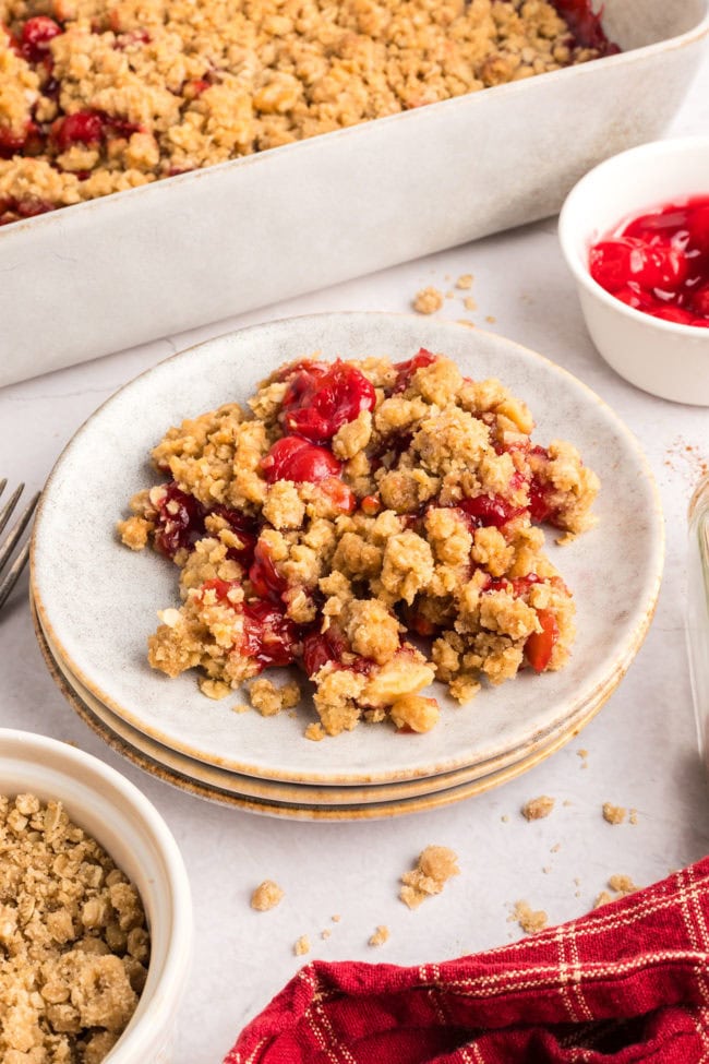 a serving of homemade cherry crumble on a plate with the full dish in the back ground.