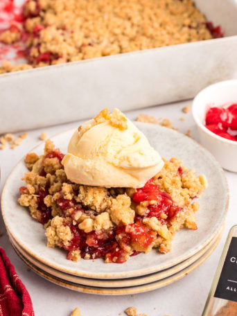 A plated serving of sweet cherry crumble with a scoop of vanilla ice cream