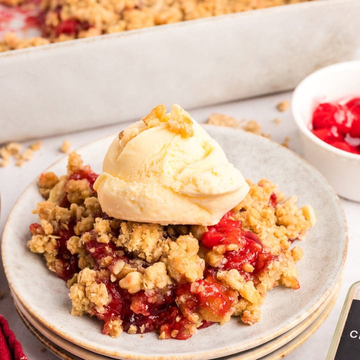 A plated serving of sweet cherry crumble with a scoop of vanilla ice cream