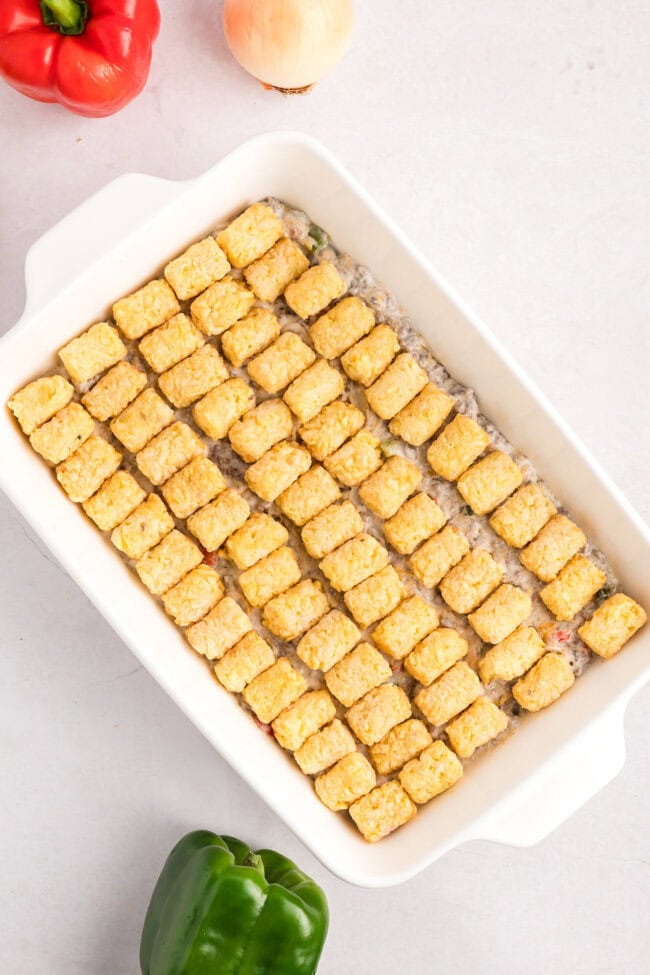 frozen tater tots over cheesy casserole in a white baking dish