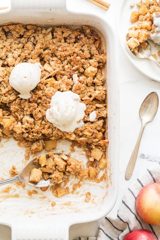 apple oatmeal crumble in a white dish with scoops of vanilla ice cream