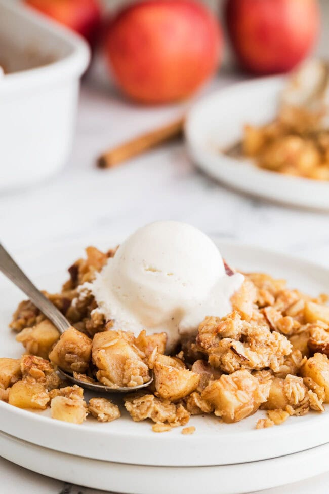 apple crumble on a plate with a spoon and a scoop of vanilla ice cream