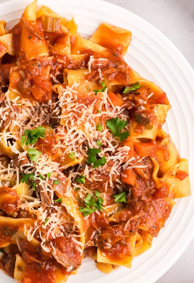 crockpot beef ragu over pasta on a white plate