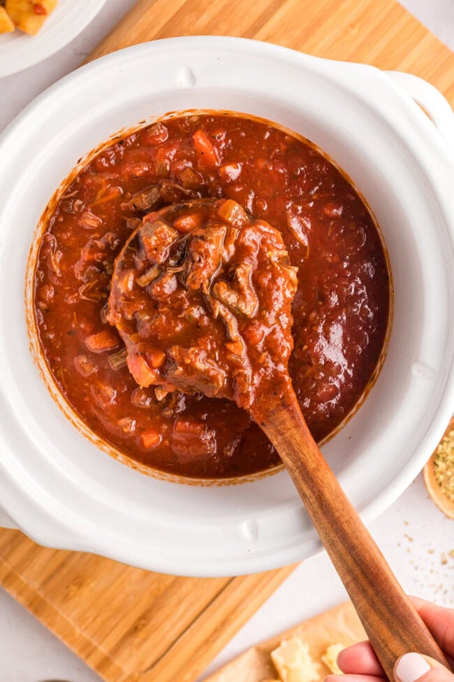 beef ragu in a slow cooker with a wooden spoon