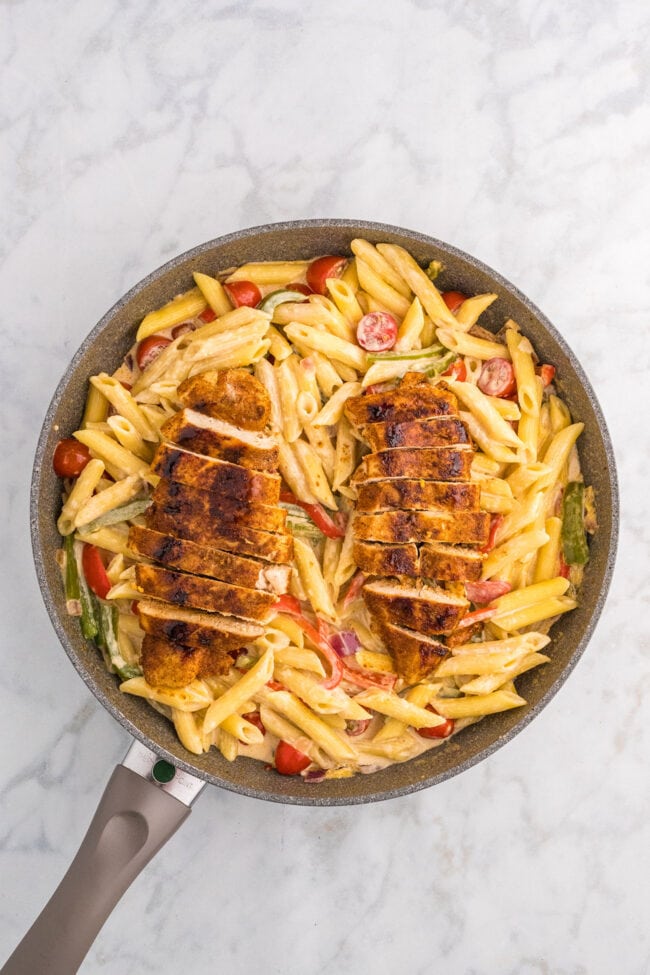 cut chicken breasts placed on top of pan of penne pasta