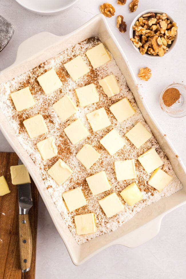 cake mix and apples in a white baking dish with pats of butter on top