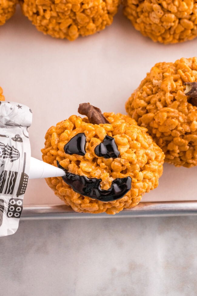 using icing to make a jack-o-lantern face on a pumpkin shaped rice krispie treat