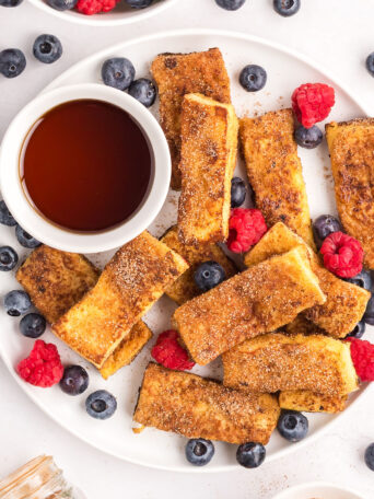 french toast sticks with a cup of syrup and fresh berries