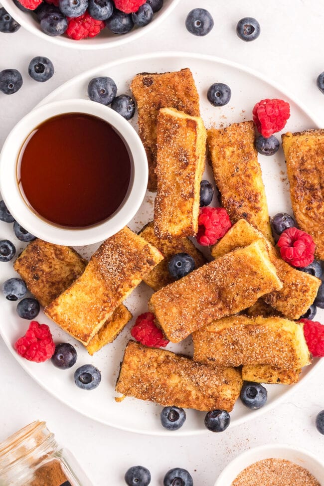 french toast sticks with a cup of syrup and fresh berries