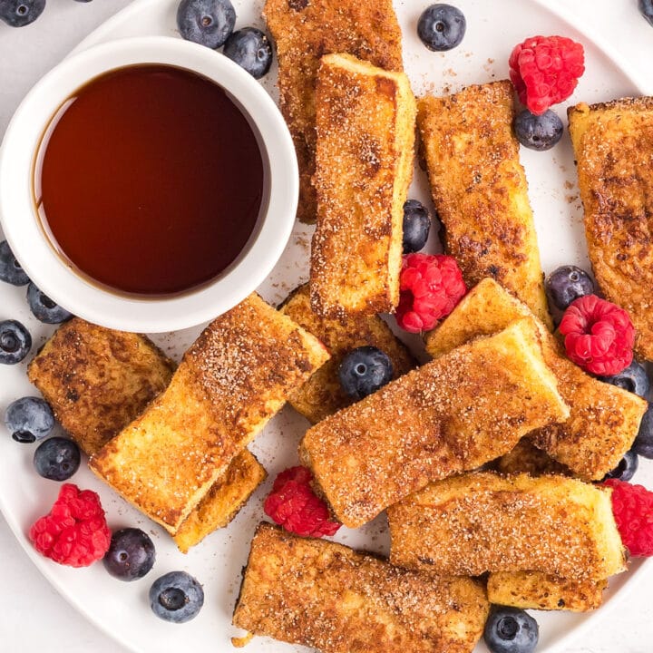 french toast sticks with a cup of syrup and fresh berries