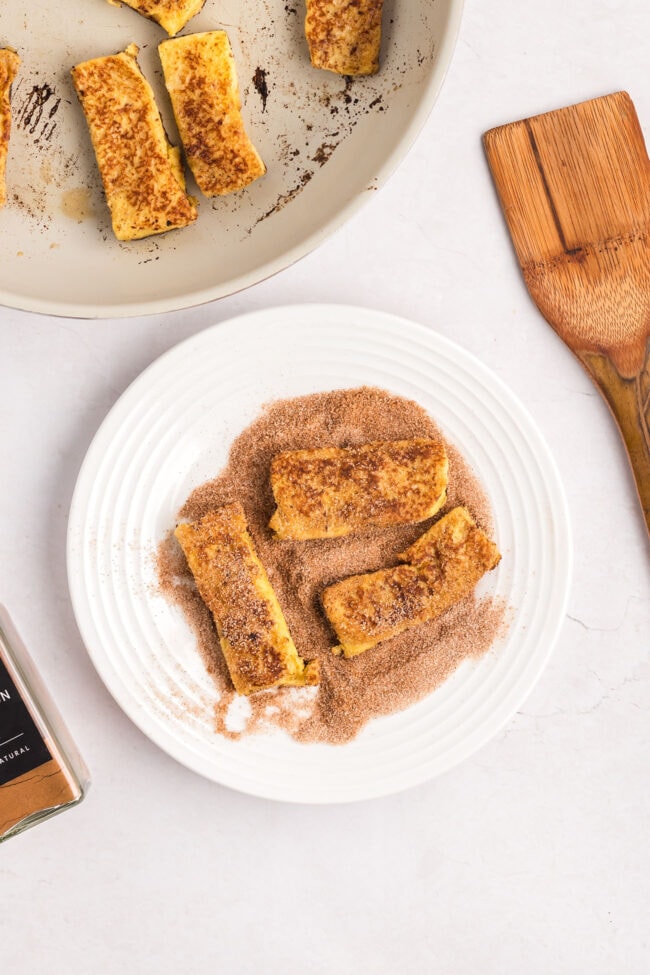 rolling warm french toast sticks in cinnamon sugar