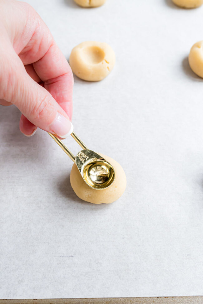 pressing the back of a measuring spoon in to a cookie ball.