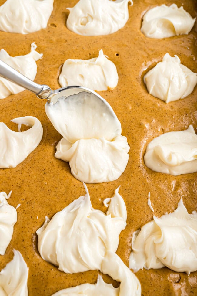 Cream cheese frosting being dolloped onto a pumpkin cake.