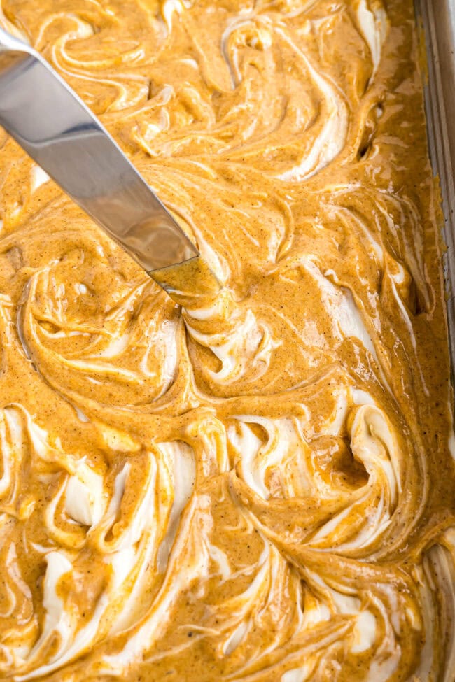 swirling cheesecake filling in a pumpkin earthquake cake batter