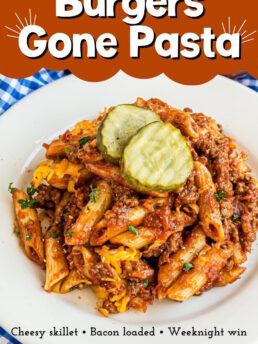Skillet of pasta mixed with ground beef, crispy bacon, and melted cheese, served with classic burger condiments on the side.