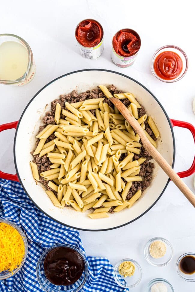Skillet with cooked ground beef and penne pasta before adding sauce for Bacon Cheeseburger Pasta Skillet.