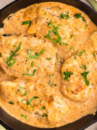 Skillet filled with creamy smothered chicken, garnished with parsley.