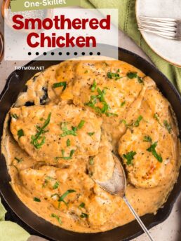 Skillet with creamy smothered chicken simmering, garnished with fresh parsley.