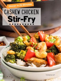 Cashew Chicken Stir Fry served over rice in a white bowl with chopsticks; colorful veggies and tender chicken in a savory-sweet sauce, skillet in the background.