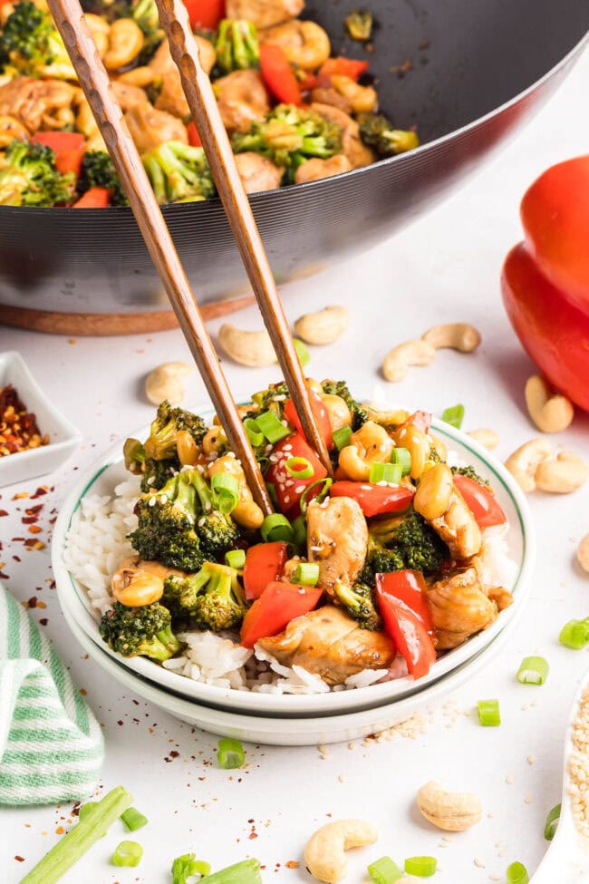 Cashew Chicken Stir Fry served over white rice with chopsticks — tender chicken, crisp vegetables, and cashews coated in a glossy, savory-sweet sauce.