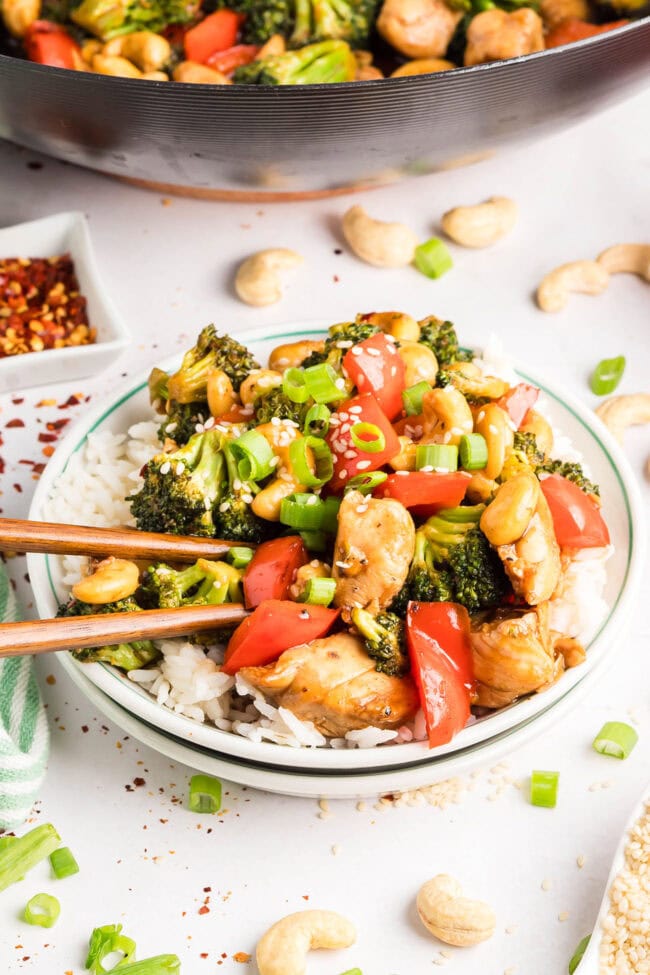 Cashew Chicken Stir Fry plated and served over white rice with chopsticks — tender chicken, crisp vegetables, and cashews coated in a glossy, savory-sweet sauce.