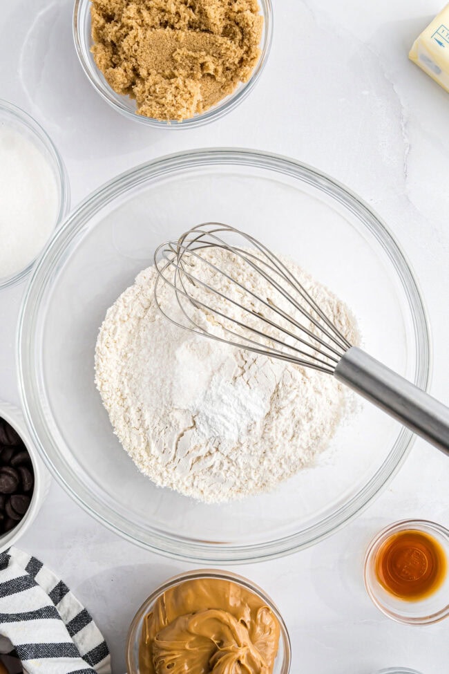 Mixing flour, baking powder, and salt in a glass bowl with a wire whisk for peanut butter blondies.