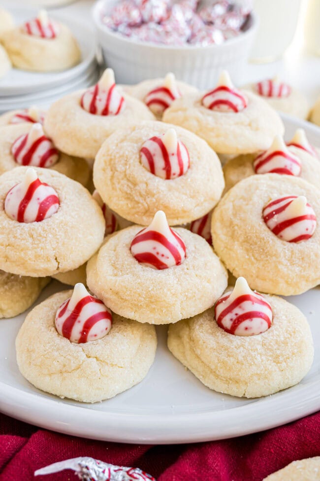 Overhead shot of Candy Cane Kiss Cookies piled on a white plate, showing the red and white peppermint Kisses.