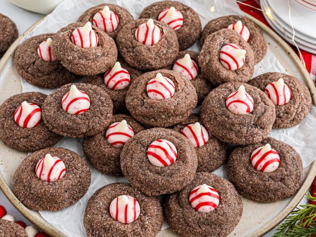 Overhead horizontal shot of Chocolate Peppermint Kiss Cookies cooling on parchment with candy cane Kisses.