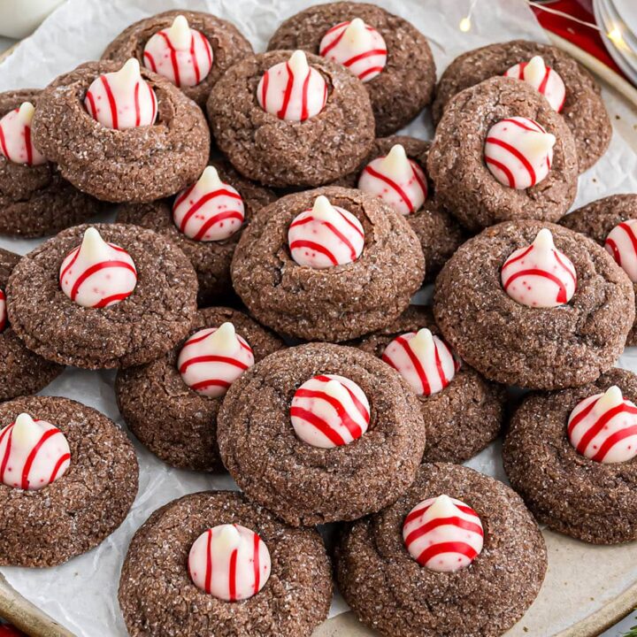 Overhead horizontal shot of Chocolate Peppermint Kiss Cookies cooling on parchment with candy cane Kisses.