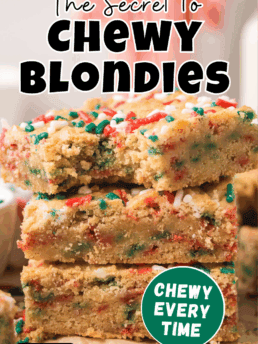 Close-up stack of chewy Christmas blondies with holiday sprinkles, with the top bar showing a bite to highlight the soft, chewy texture.