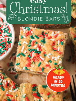 Soft and chewy Christmas blondie bars stacked with a bowl of festive sprinkles beside them, an easy holiday dessert bar for cookie trays.