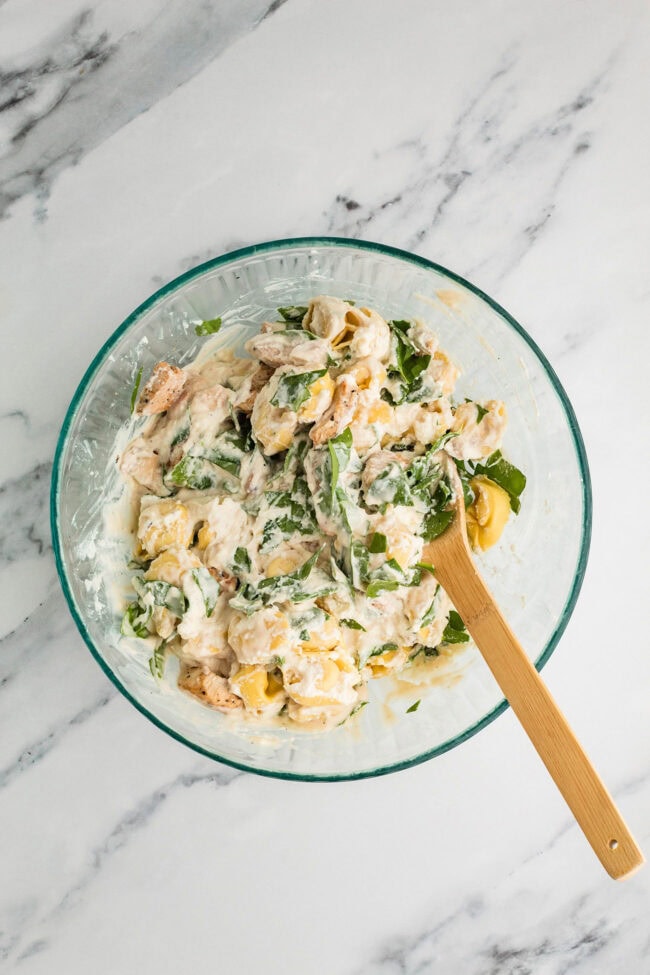 Chicken Tortellini Casserole ingredients being mixed together in a glass bowl before baking.