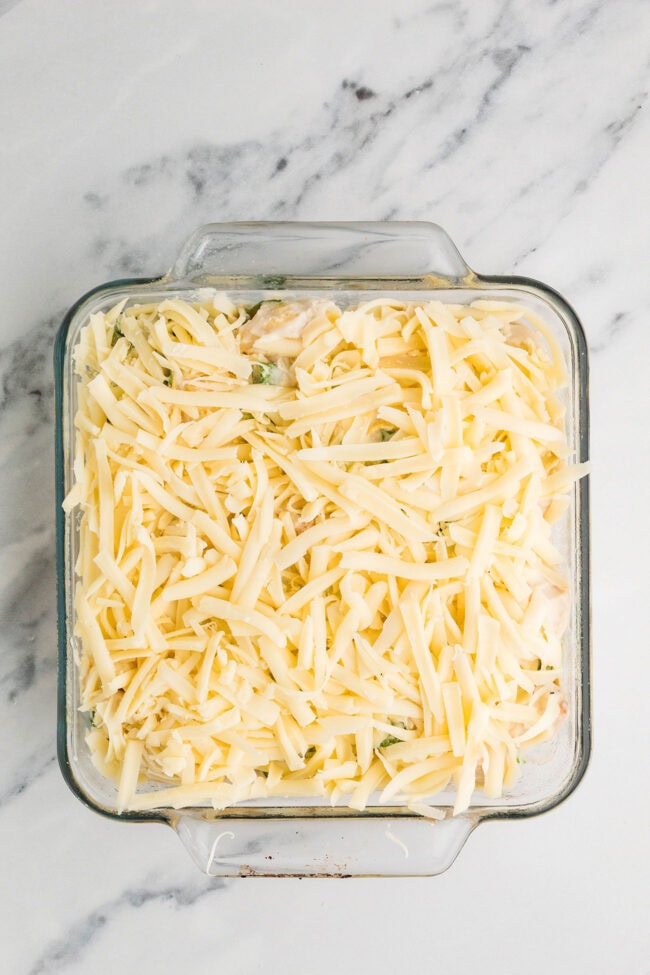 Unbaked Chicken Tortellini Casserole in a square glass baking dish and topped with shredded cheese.