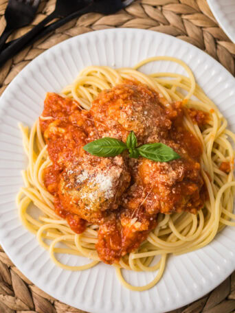 Chicken Parmesan meatballs served over spaghetti with marinara sauce, melted mozzarella, and fresh basil.