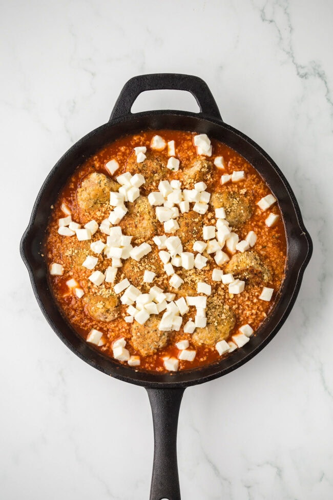 Chicken meatballs in marinara sauce topped with diced mozzarella before baking.